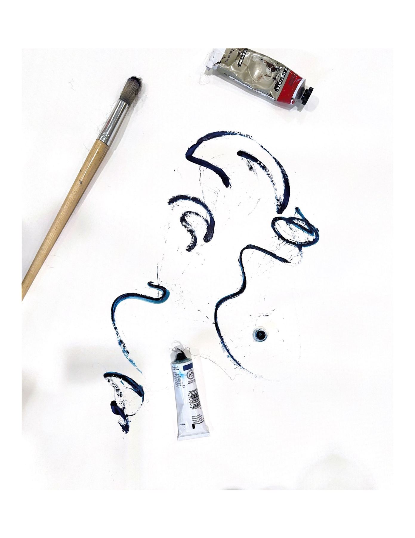 Blue ink strokes beside a brush and paint tubes